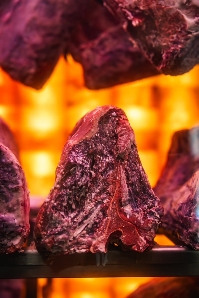 Meat Dry Aging Room with wall of pink Himalayan salt. Dry-Aged meat cuts with a lit Himalayan salt wall on the background.